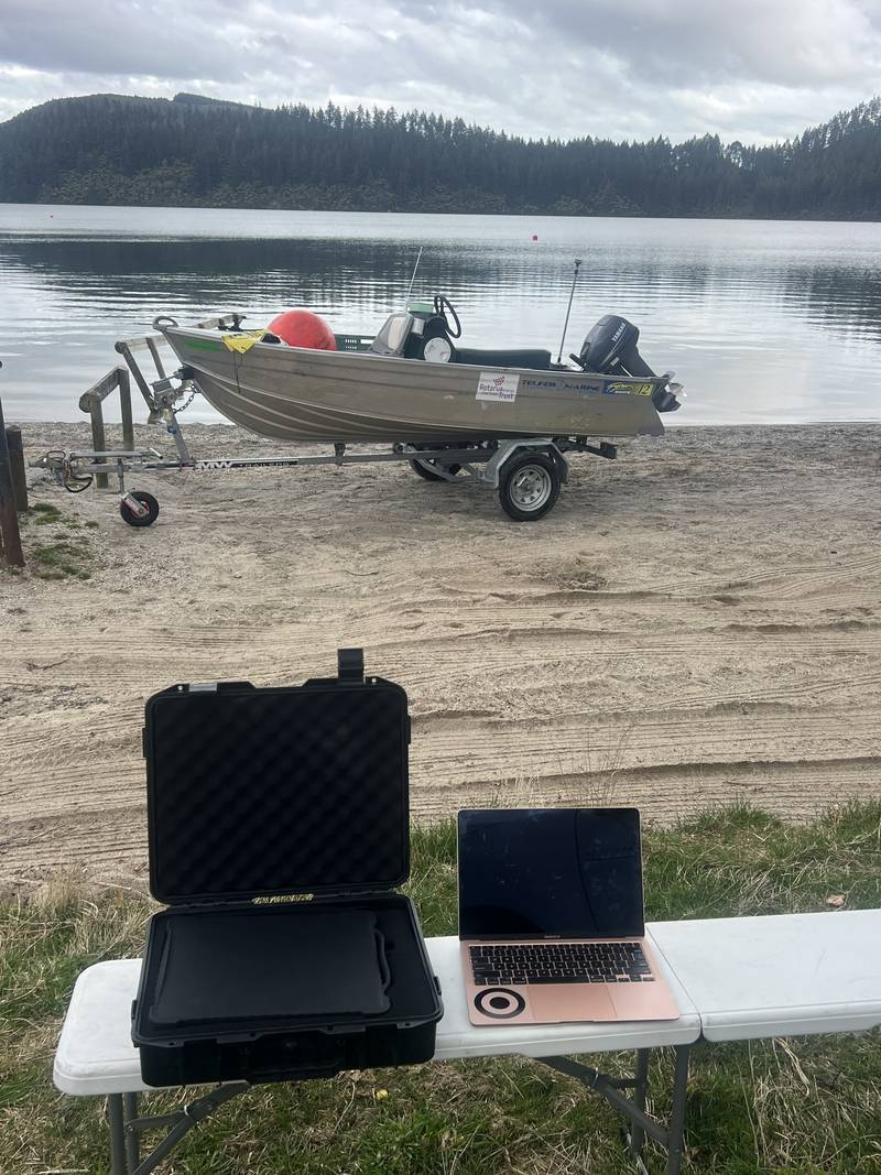 A dinghy on its trailer at the lake edge, with the Starlink Mini case and a laptop on a table