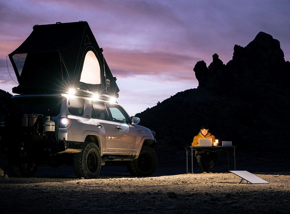A four-wheel drive with a rooftop tent at dusk, someone working at a table with a Starlink Mini